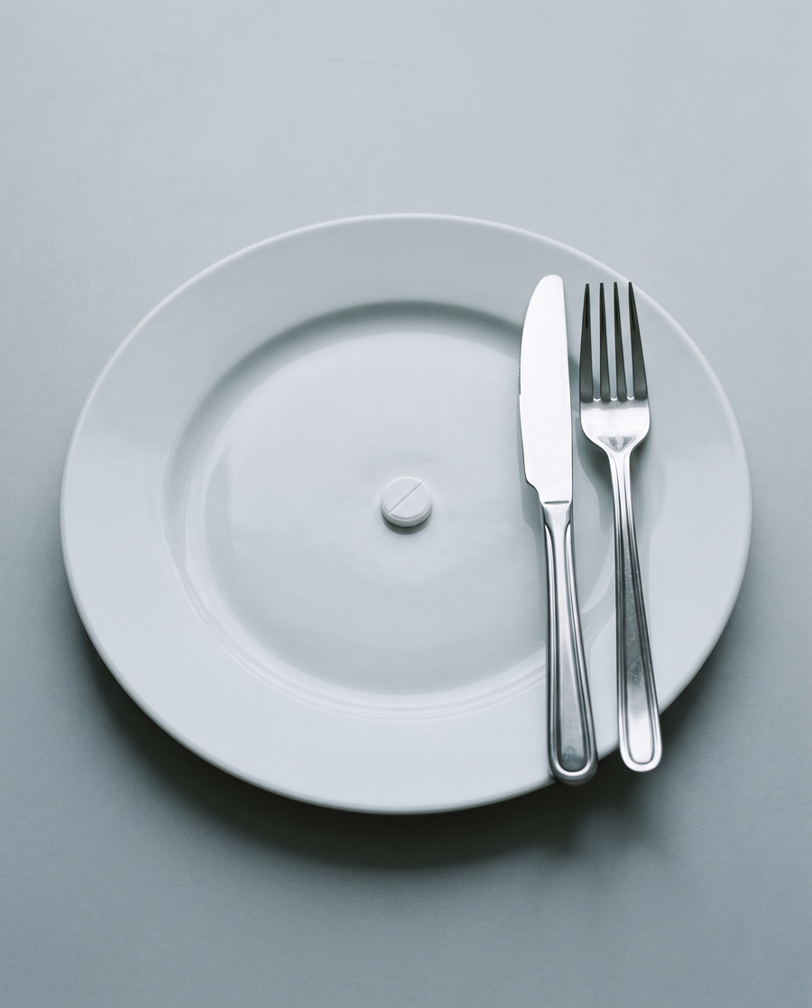 A single pill alone on an empty white plate, in grey light